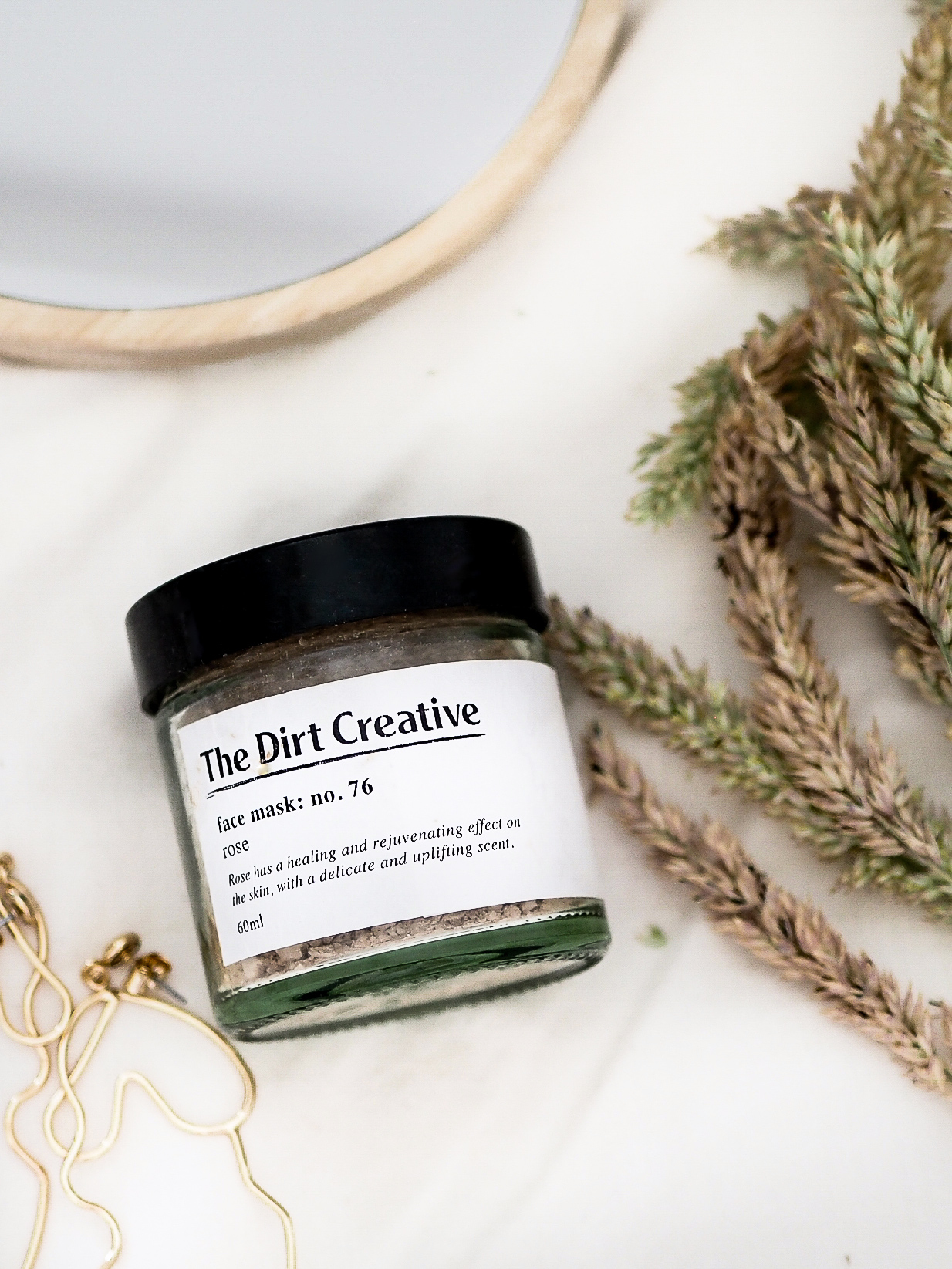 the dirt creative rose and pink clay face mask, flatlay with dried grass and wooden mirror
