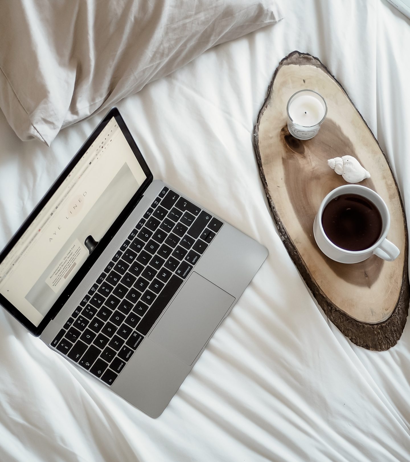 laptop on bed with candle and coffee
