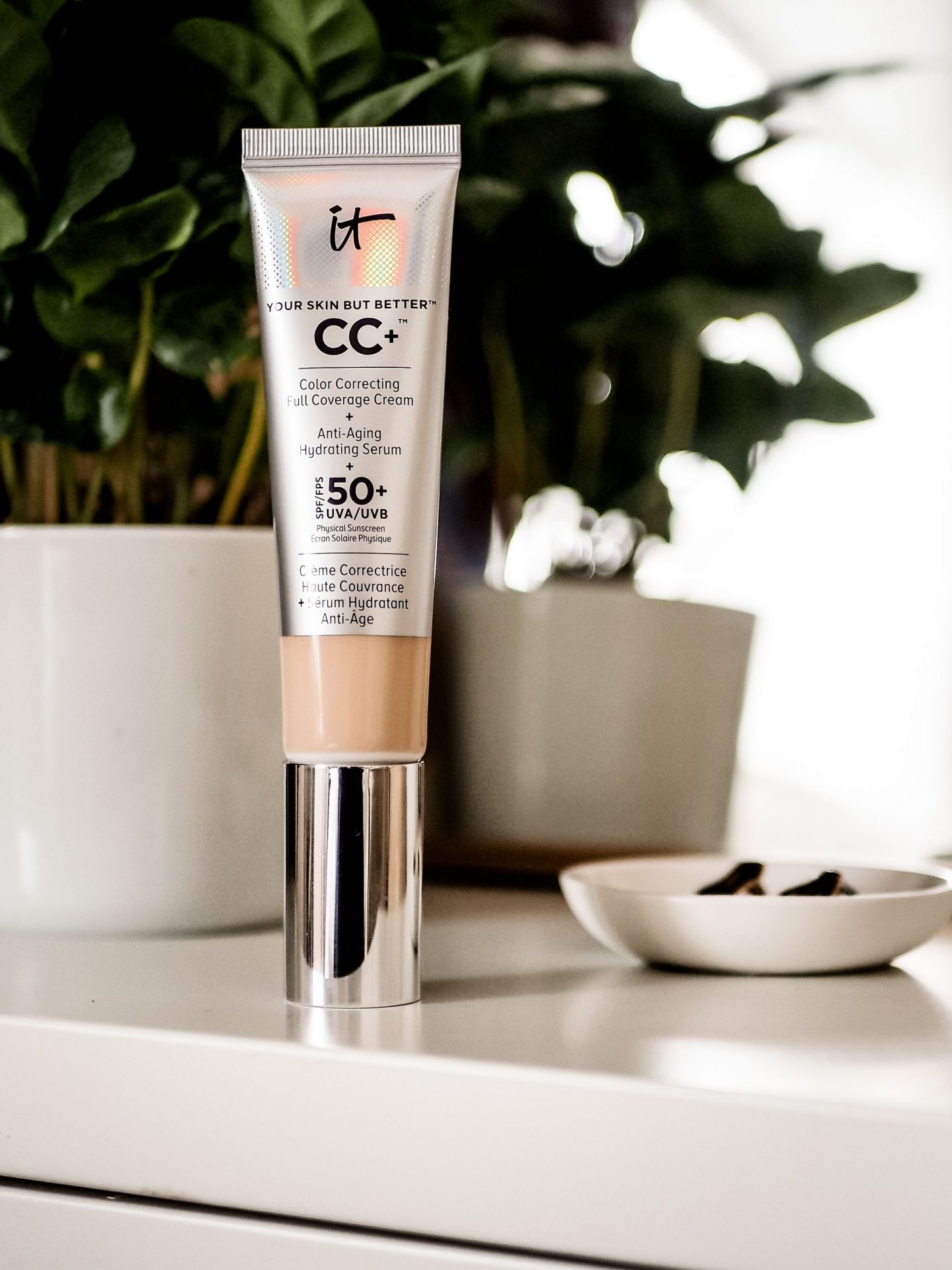 IT CC Full coverage cream sitting on dresser with mirror and plant