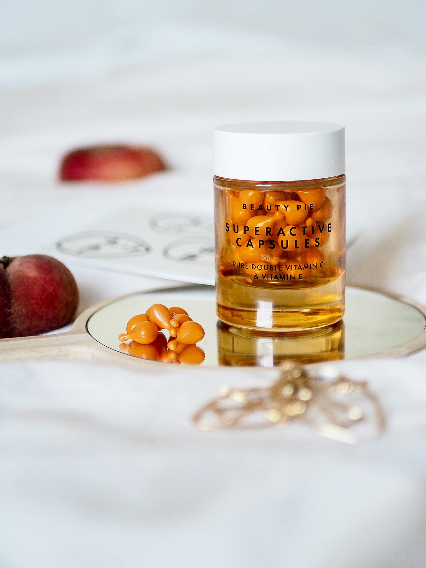 beauty pie vitamin c capsules sitting on mirror with peaches