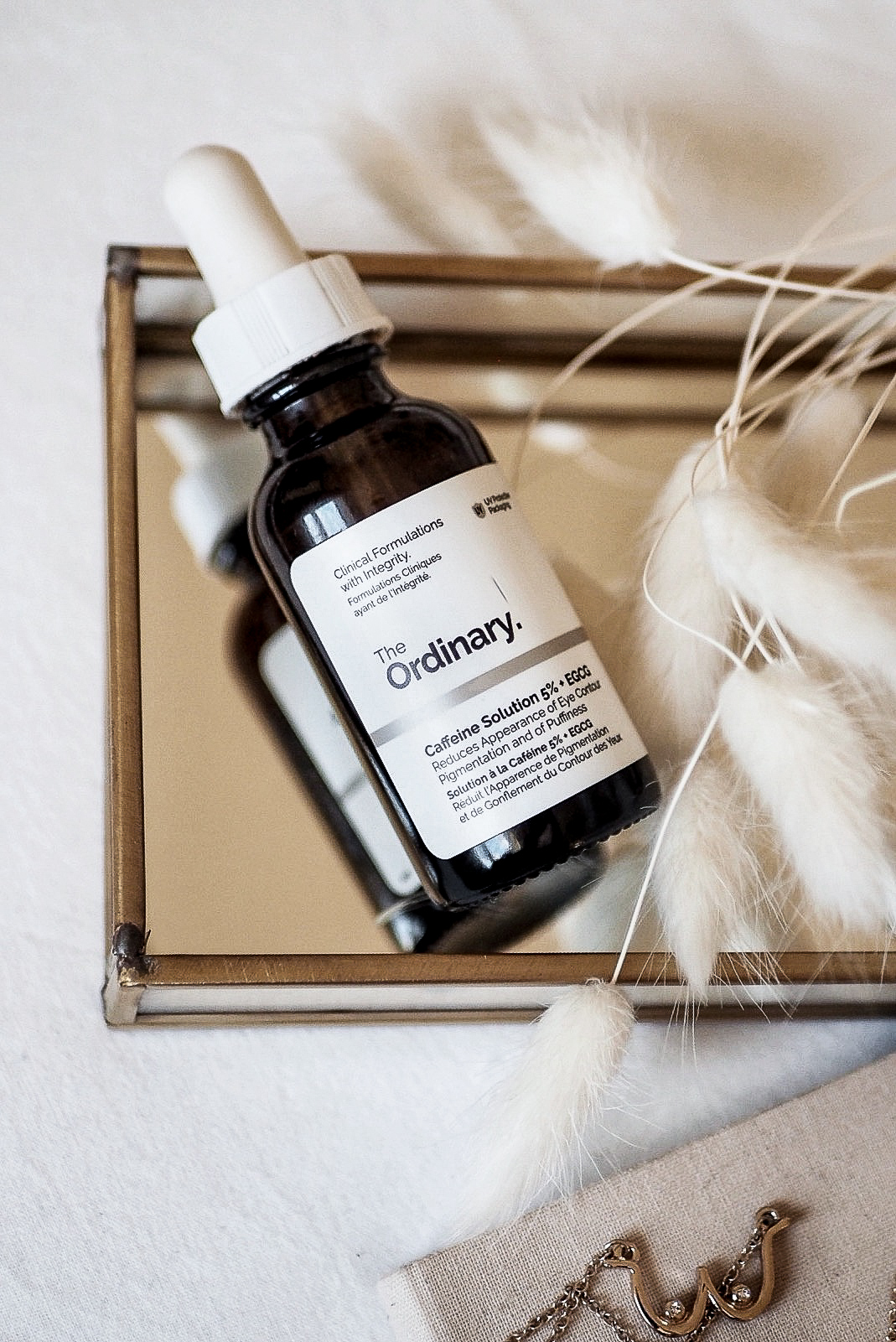 the ordinary caffeine solution sitting on mirrored tray with bunny ear dried grass